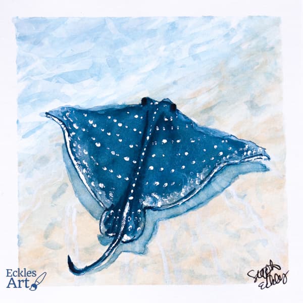 An indigo stingray with a pattern of white dots across its back gently glides over the sandy ocean floor in the shallows.