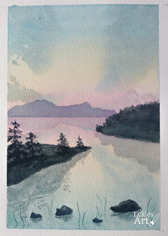 A serene mountain lake at sunset, with a beautifully tranquil atmosphere. The scene features a calm body of water reflecting the cool hues of the setting sun, creating a gradient of colors in the sky—ranging from soft pinks and oranges to blues. A hint of mountains rise in the background, their silhouettes adding depth and contrast to the composition. The middle ground shows two opposing triangular slices of land jutting into the lake, with the left bank hosting four evergreen trees. The trees are gently reflected. The foreground concludes with a few stony rocks peeking above the water as well as a smattering of reeds, and the reflection thereof.